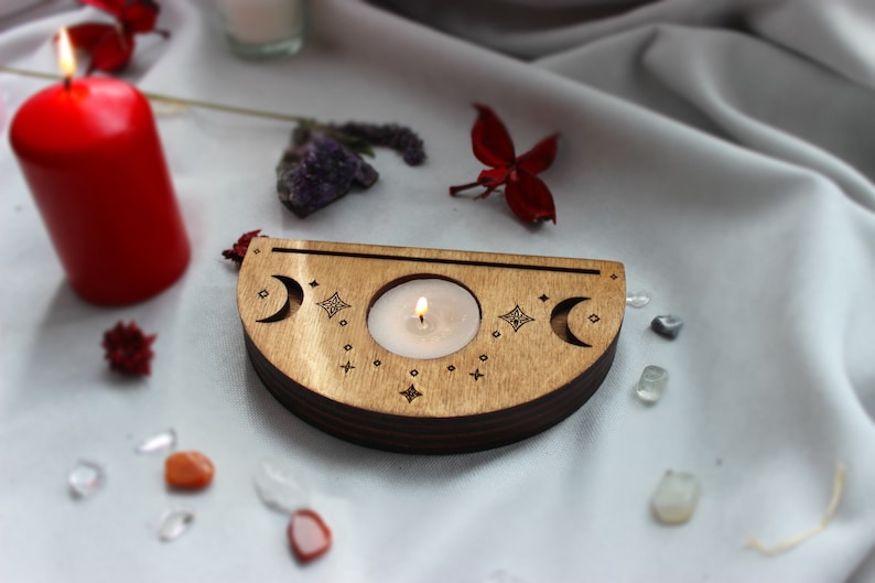 May include: A wooden candle holder with a crescent moon design and stars. A small white candle is burning in the center of the holder.