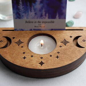 May include: Wooden candle holder with a crescent moon design and a small candle burning inside. The holder has a slot for a card that reads "Believe in the impossible of Blue Moon".