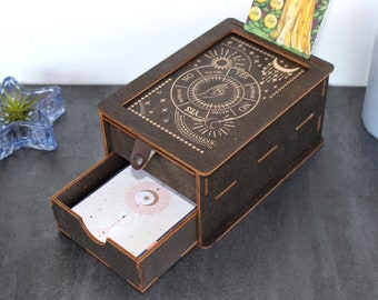 May include: A wooden box with a drawer, featuring a celestial design with a sun, moon, and stars. The box has a sliding top with a "Yes/No/Maybe" wheel and a card slot. The drawer is open, revealing a card with a celestial design.