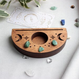 May include: A wooden crescent moon shaped tray with three small green stones and a carved design of moons and stars.