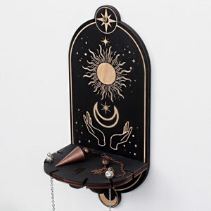 May include: Black wooden wall shelf with a sun, moon, and stars design. The shelf has a small ledge for displaying items like crystals or jewelry.