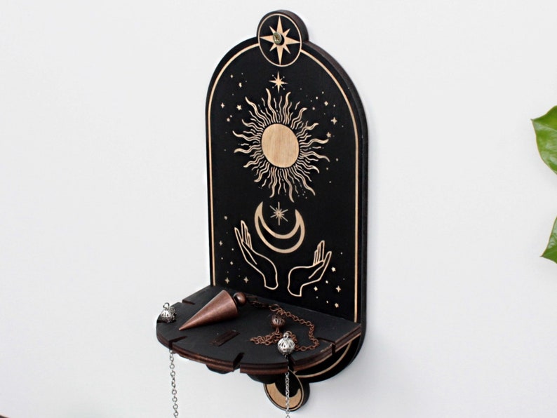 May include: Black wooden wall shelf with a sun, moon, and stars design. The shelf has a small ledge for displaying items like crystals or jewelry.