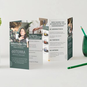 May include: A product display featuring a brochure about essential oils, with the dōTERRA logo. The brochure is open, revealing text and images. A green glass vase holds green pencils, and a white mug is on the left.