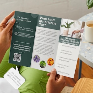 May include: A person holding a brochure with text in German about essential oils. The brochure is open, displaying information and images of lavender, mint, and oranges. A QR code is visible. A cup of coffee and a small plant are in the background.