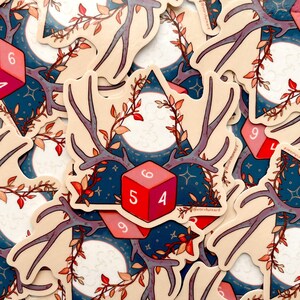 Pu&ograve; includere: Un adesivo con un dado rosso e bianco con i numeri 5, 4 e 6. Il dado &egrave; circondato da corna, foglie e una luna crescente su uno sfondo blu.