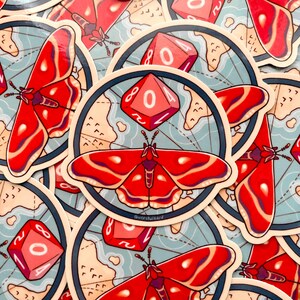 Pu&ograve; includere: Un set di adesivi con una falena rosso e nero con una mappa stilizzata e un dado rosso e bianco con il numero 04. Gli adesivi sono su uno sfondo blu con accenti bianchi.