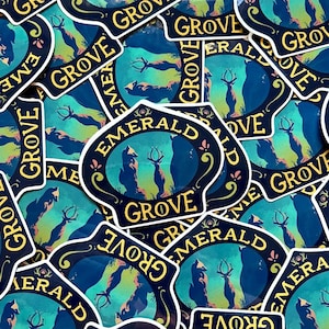 May include: A close-up of several stickers featuring a blue and yellow design with the text "Emerald Grove". The design features a fox and a deer standing in a forest setting.