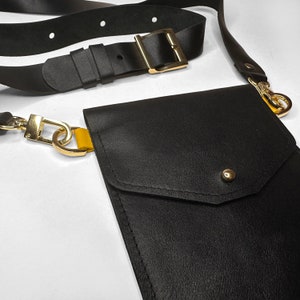 May include: A black leather crossbody bag with a gold chain and a flap closure. The bag has a small pocket on the front.