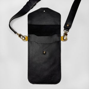 May include: Black leather crossbody phone bag with a gold clasp and strap. The bag has a flap closure and a small pocket on the front.