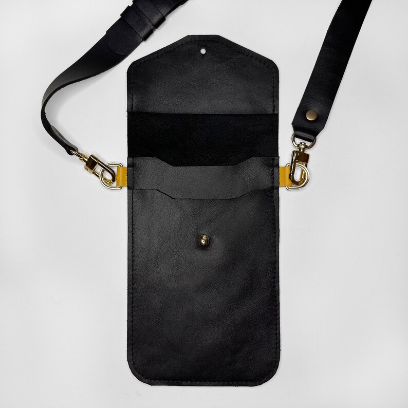 May include: Black leather crossbody phone bag with a gold clasp and strap. The bag has a flap closure and a small pocket on the front.