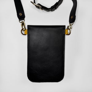 May include: Black leather crossbody bag with a gold buckle and strap. The bag has a flap closure and a small pocket on the front.
