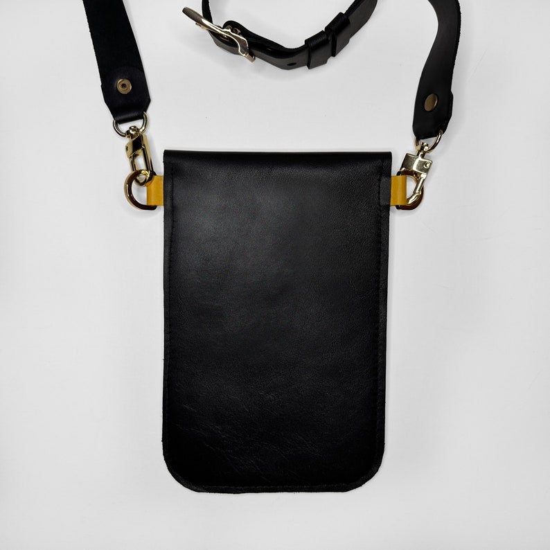 May include: Black leather crossbody bag with a gold buckle and strap. The bag has a flap closure and a small pocket on the front.