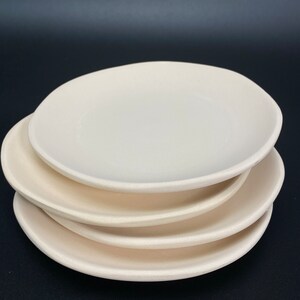 May include: A stack of four plain white ceramic plates. The plates are round and have a slightly uneven edge.