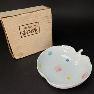 May include: A white ceramic apple-shaped bowl with a leaf handle. The bowl has a light blue, pink, and yellow polka dot design. The bowl is in a cardboard box with the text "伝統と創造" in Japanese characters.