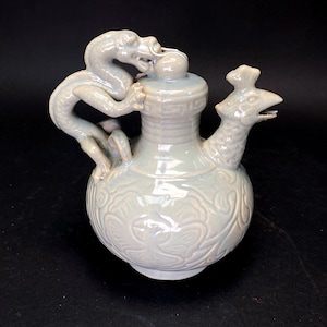 Puede incluir: Una tetera de cerámica esmaltada en color celadón pálido con un asa de dragón y un pico en forma de pájaro. El cuerpo de la tetera es redondo con patrones florales en relieve. El dragón envuelve la tapa.