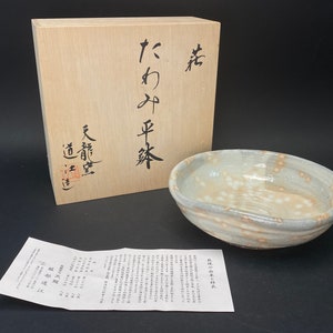 Könnte beinhalten: Eine weiße Keramikschale mit gesprenkeltem Glase und eine Holzkiste mit japanischen Schriftzeichen. Die Kiste trägt die Aufschrift "Takayama Sencha" und "Dozen"