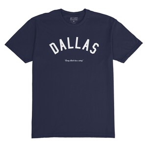 Puede incluir: Una camiseta azul marino con un gr&aacute;fico blanco en arco "DALLAS" y el texto "Every block has a story" debajo. La camiseta est&aacute; hecha por Allies.