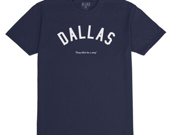 Op de afbeelding: Een marineblauw t-shirt met een witte gebogen "DALLAS" grafische afbeelding en de tekst "Every block has a story" eronder. Het shirt is gemaakt door Allies.