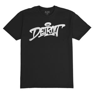 Puede incluir: Camiseta negra con un gráfico blanco de la palabra "DETROIT" en estilo graffiti.