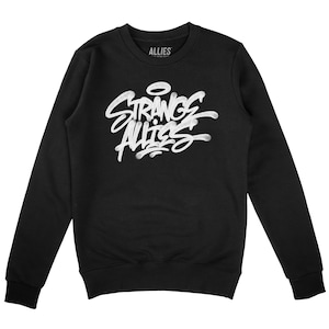 Può includere: Felpa nera con una stampa grafica bianca che dice "Strange Allies" in stile graffiti.