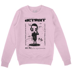 Peut inclure: Sweat-shirt rose &agrave; manches longues avec un imprim&eacute; graphique noir d'un personnage de dessin anim&eacute; avec le texte "DETROIT" et "ESTAMOS TODOS JUNTOS EN ESTO" et "&iquest;POR QUE NO HACEN UNA FIESTA?"