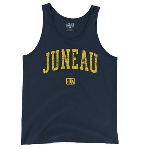 May include: Navy blue tank top with the word "JUNEAU" in distressed yellow lettering. Below the word "JUNEAU" is the number "907" in a yellow rectangle. The tank top has a classic, sleeveless design.