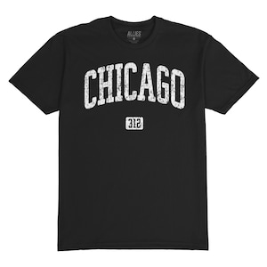 Puede incluir: Camiseta negra con la palabra "CHICAGO" en letras blancas desgastadas arqueadas sobre el pecho. Debajo de la palabra "CHICAGO" está el número "312" en una fuente blanca más pequeña. La camiseta tiene cuello redondo y mangas cortas.