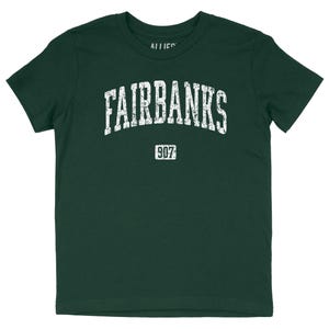 May include: A dark green t-shirt with a white distressed print of "FAIRBANKS" in an arched font and "907" below it.