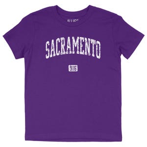 Puede incluir: Camiseta de manga corta de color morado con un gráfico blanco de estilo vintage que dice "SACRAMENTO" con el número "916" debajo.
