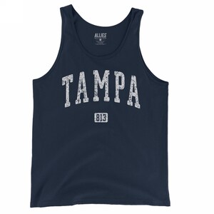 May include: Navy blue tank top with the word "TAMPA" in distressed white lettering across the chest, with "813" below. The tank top is a sleeveless shirt, perfect for warm weather.