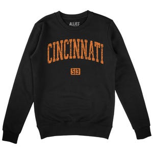 May include: Black crew neck sweatshirt featuring the word "CINCINNATI" in distressed orange lettering. Below the word is the number "513" in a rectangular box. The brand name "ALLIES" is printed above the word "CINCINNATI".