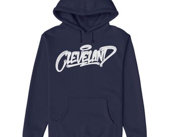 May include: A navy blue hooded sweatshirt with a white graphic of the word "CLEVELAND" in a graffiti style.