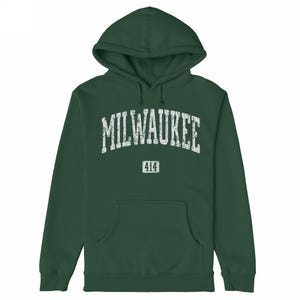 May include: A dark green hooded sweatshirt with a front pocket. The word "MILWAUKEE" is printed across the chest in distressed white lettering, with "414" below it. The hoodie is made of a soft material.