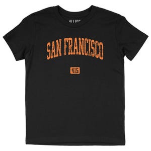 Op de afbeelding: Zwart T-shirt met de tekst "SAN FRANCISCO" in verweerde oranje letters op de borst. Daaronder het nummer "415" in een oranje kader. De t-shirt heeft een ronde hals.