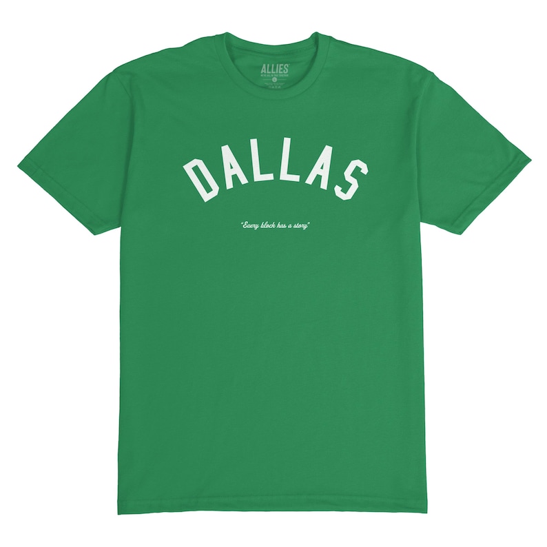 Puede incluir: Camiseta verde con texto blanco que dice "Dallas" en una fuente arqueada. El texto "Every block has a story" est&aacute; impreso en una fuente m&aacute;s peque&ntilde;a debajo de la palabra Dallas.