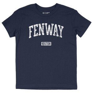 May include: Navy blue t-shirt with the word "FENWAY" in distressed white lettering, arched across the chest. Below, the word "BOSTON" is printed in a rectangular box. The shirt is a classic crew neck style.