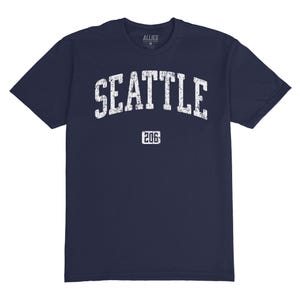 May include: Navy blue t-shirt with a white distressed graphic that says "SEATTLE" in an arch with "206" underneath.