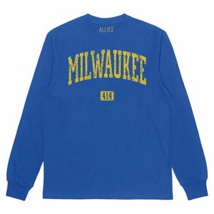 May include: A long-sleeved blue shirt with the word "MILWAUKEE" in distressed yellow lettering across the chest. Below the word "MILWAUKEE" is the number "414" in a yellow rectangle. The word "ALLIES" is printed above the word "MILWAUKEE".
