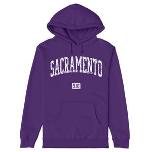 Puede incluir: Sudadera con capucha morada con un gráfico blanco desgastado que dice "SACRAMENTO" con el número "916" debajo.
