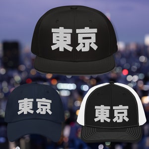 May include: Three baseball caps with the word "Tokyo" written in Japanese characters on the front. The caps are black, navy blue, and black with a white mesh back.