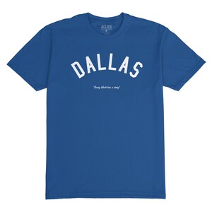 Puede incluir: Una camiseta azul real con un dise&ntilde;o de arco blanco que dice "DALLAS" y el texto "Every block has a story" debajo.