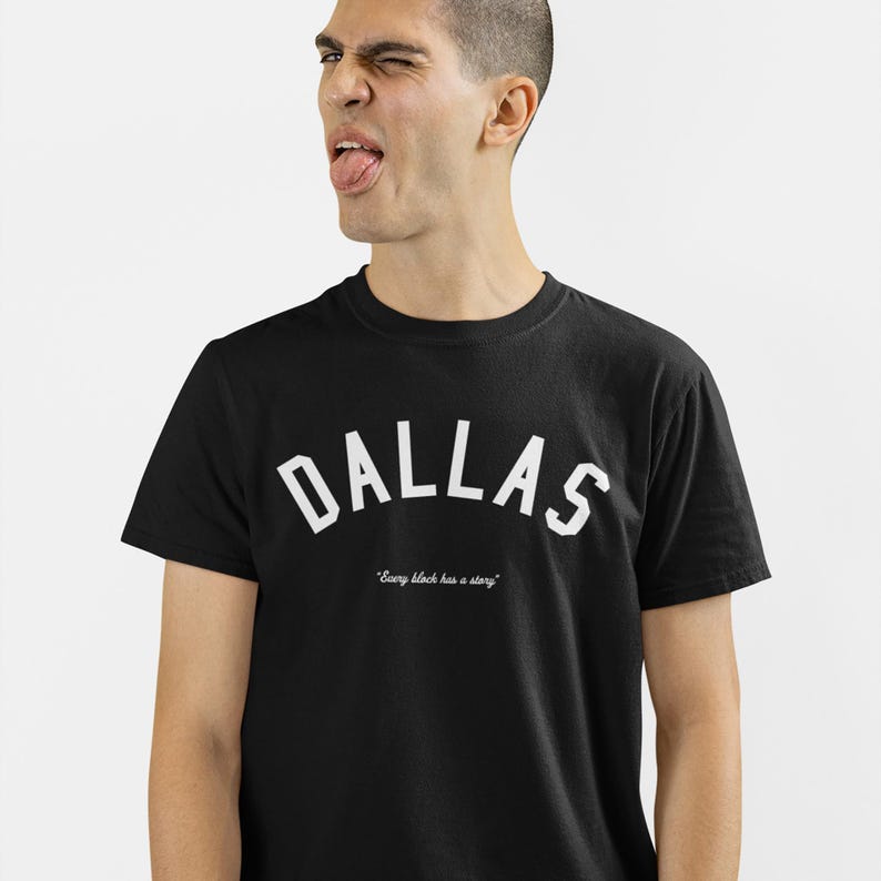 Puede incluir: Camiseta negra con texto blanco que dice "DALLAS" en una fuente arqueada. Debajo del texto hay un texto blanco m&aacute;s peque&ntilde;o que dice "Every block has a story."