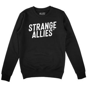 Könnte beinhalten: Schwarzes Sweatshirt mit Rundhalsausschnitt und dem Text "STRANGE ALLIES" in großen weißen Buchstaben auf der Brust. Das Wort "ALLIES" ist ebenfalls weiß auf dem oberen Rücken des Sweatshirts aufgedruckt. Das Sweatshirt hat lange Ärmel und einen gerippten Kragen und Bündchen.