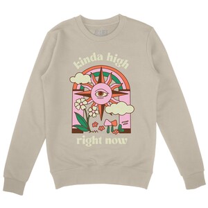 Puede incluir: Una sudadera de color beige claro con un estampado gr&aacute;fico de un sol con un ojo, un arco&iacute;ris, nubes, flores y setas. El texto "kinda high right now" est&aacute; impreso debajo del gr&aacute;fico.