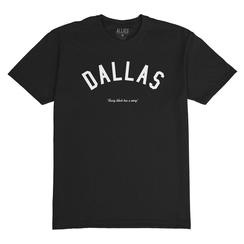 Puede incluir: Camiseta negra con texto blanco que dice "DALLAS" en una fuente arqueada. Debajo del texto est&aacute; la frase "Every block has a story."