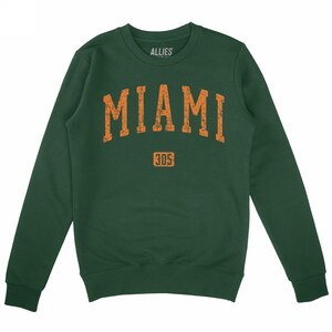 May include: A green sweatshirt featuring the word "MIAMI" in orange, arched across the chest. Below the word "MIAMI" is the number "305" in orange. The brand name "ALLIES" is printed in white at the top.