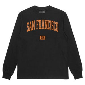 Op de afbeelding: Zwart longsleeve t-shirt met een oranje grafische print van "SAN FRANCISCO" in een boog met "415" eronder. Het shirt heeft een ronde hals en een relaxte pasvorm.