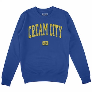 May include: A royal blue crew neck sweatshirt with long sleeves. The front features the text "CREAM CITY" in distressed yellow lettering above the number "414". The brand name "ALLIES" is printed above the text.