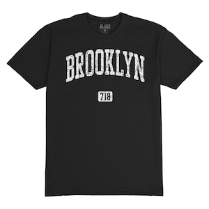 May include: Black t-shirt with a white vintage-style graphic that says "Brooklyn" with the area code "718" underneath.