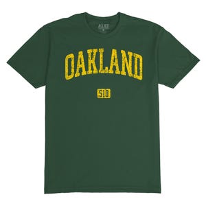 Könnte beinhalten: Ein dunkelgrünes T-Shirt mit einer gelben Grafik im Vintage-Stil, auf dem "Oakland 510" steht.